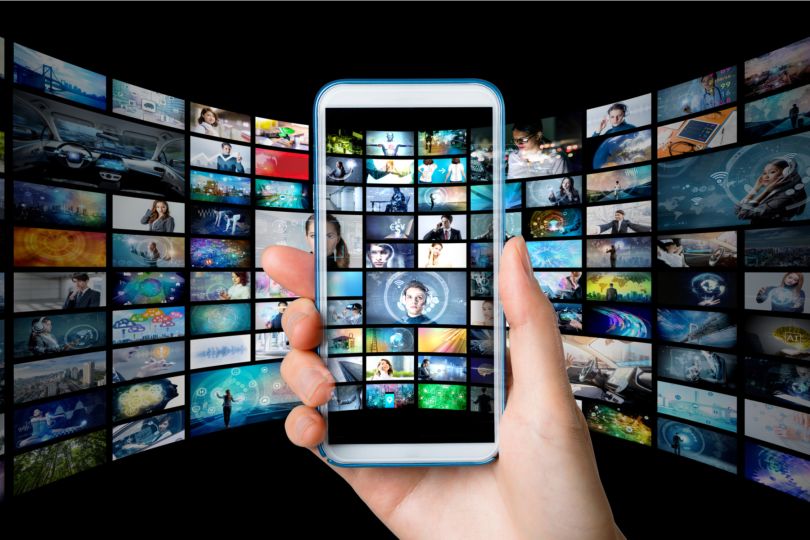 Person holds smartphone with video icons floating behind it
