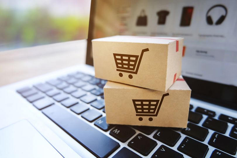 Two parcels with shopping cart icons on them sit atop a laptop.