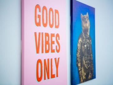Photo of outdPhoto of two wall canvas pictures, closest one says "Good Vibes Only"oor balcony area with tables and people gathered in distance