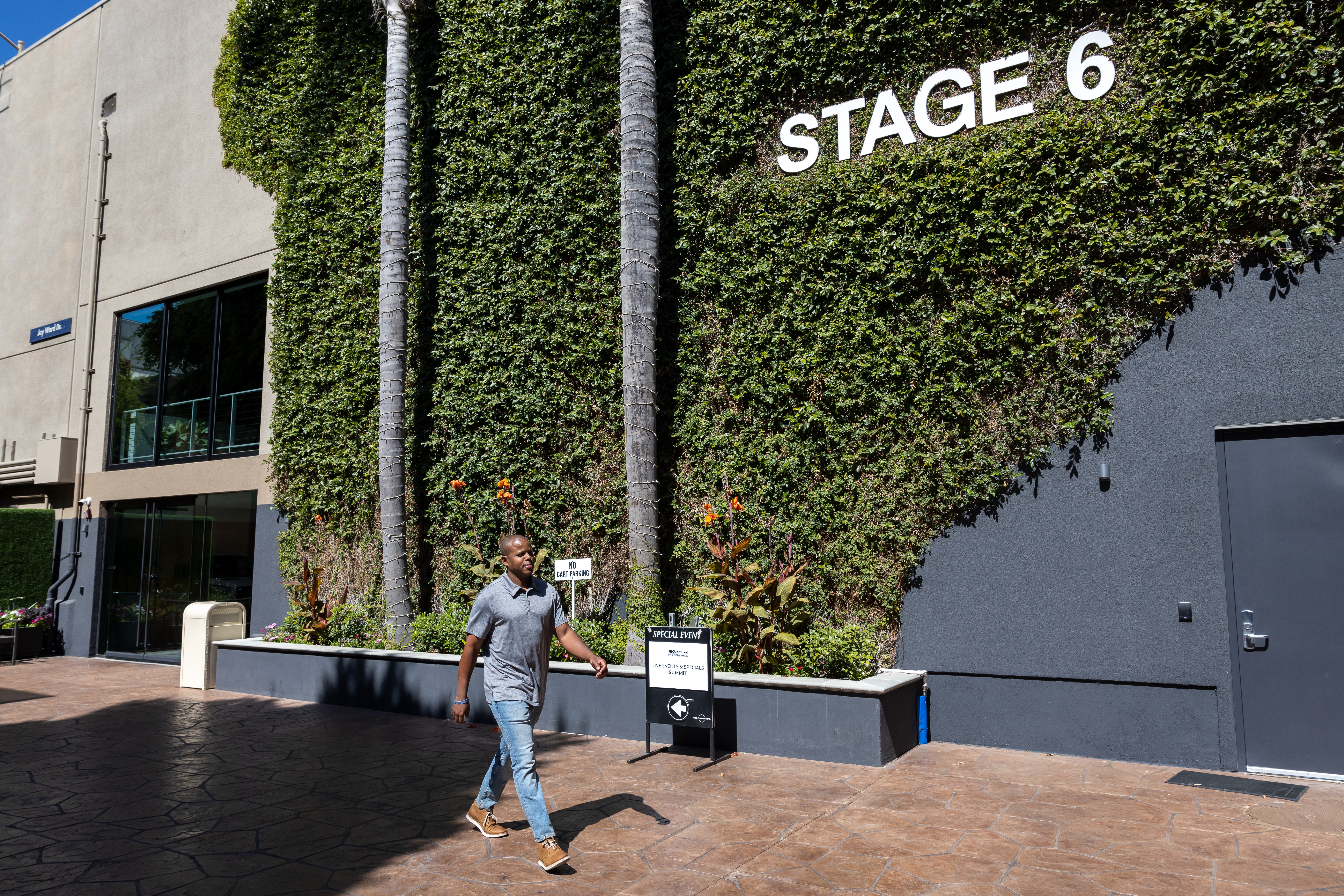 Photo of an employee walking alongside NBCUniversal_s _Stage 6_ building covered in ivy, toward door