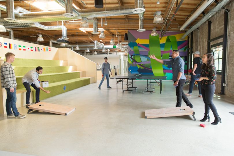 Group of young professionals play beanbag toss in open space office