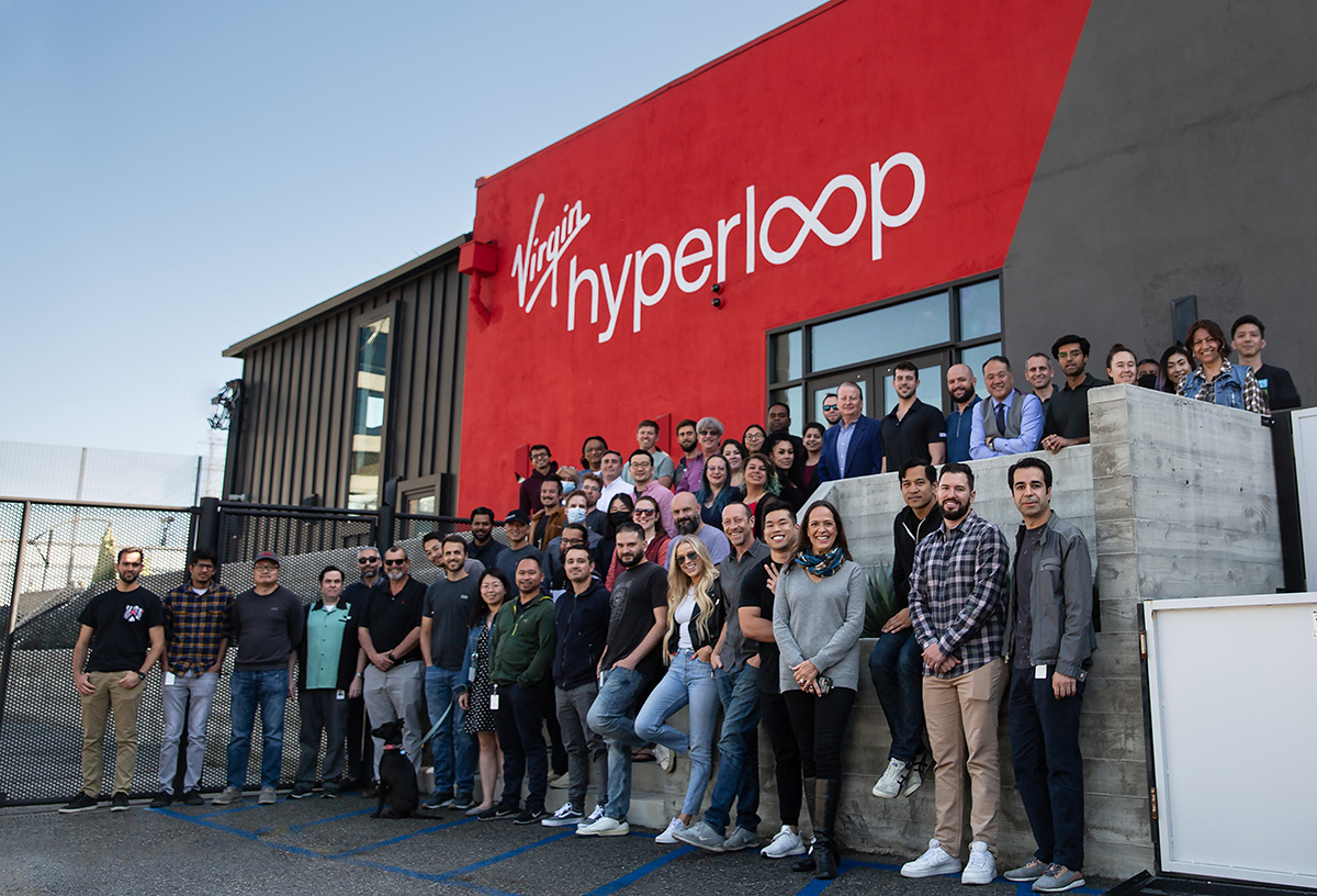 HyperloopOne team photo outside of office building with company logo on the wall behind them