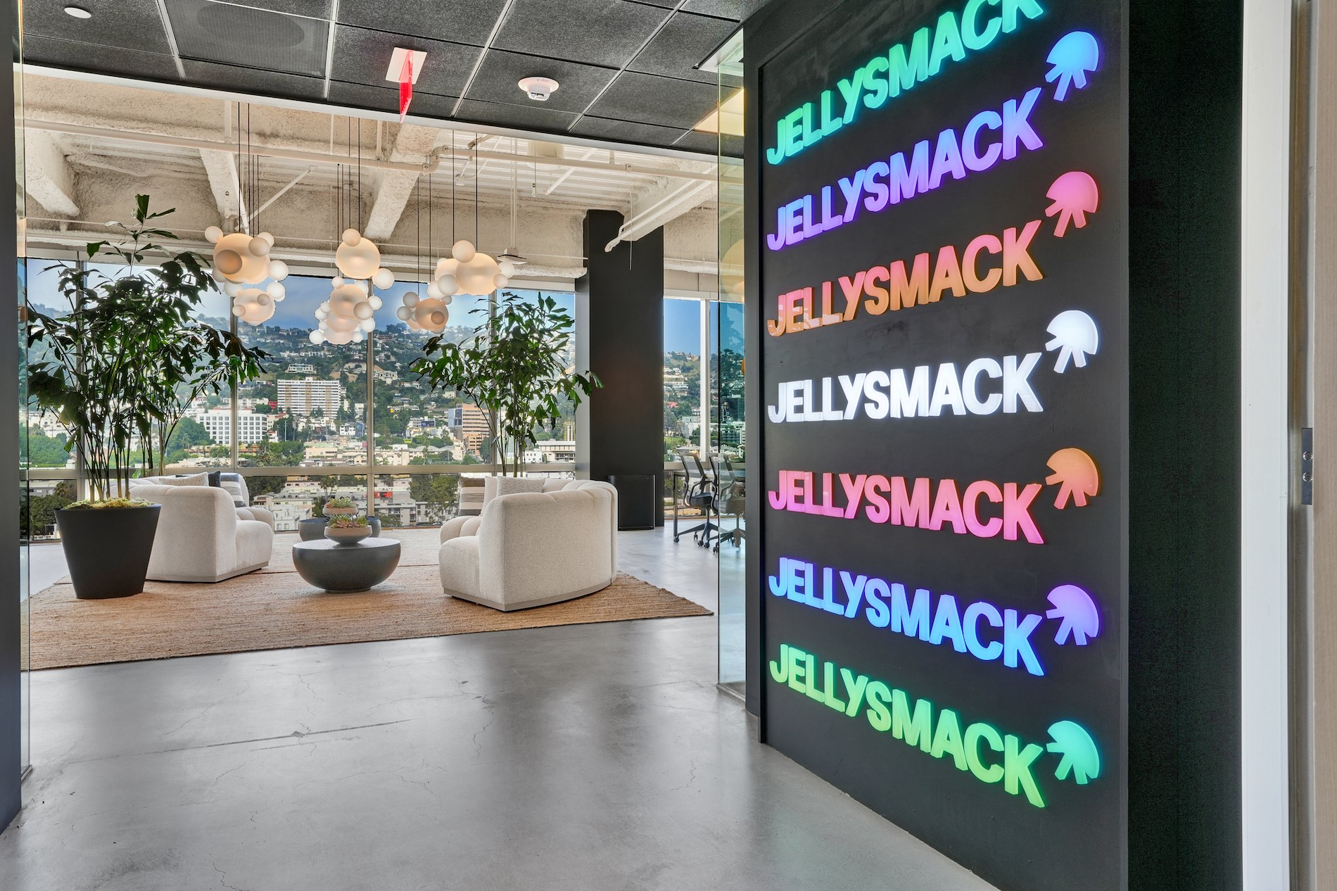 jellysmack office the logo runs up and down the wall to the right and we can see a beautifully designed seating area in the background with white furniture and indoor plants
