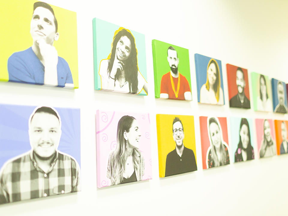 Colorful pictures of MuteSix staff hanging on office wall