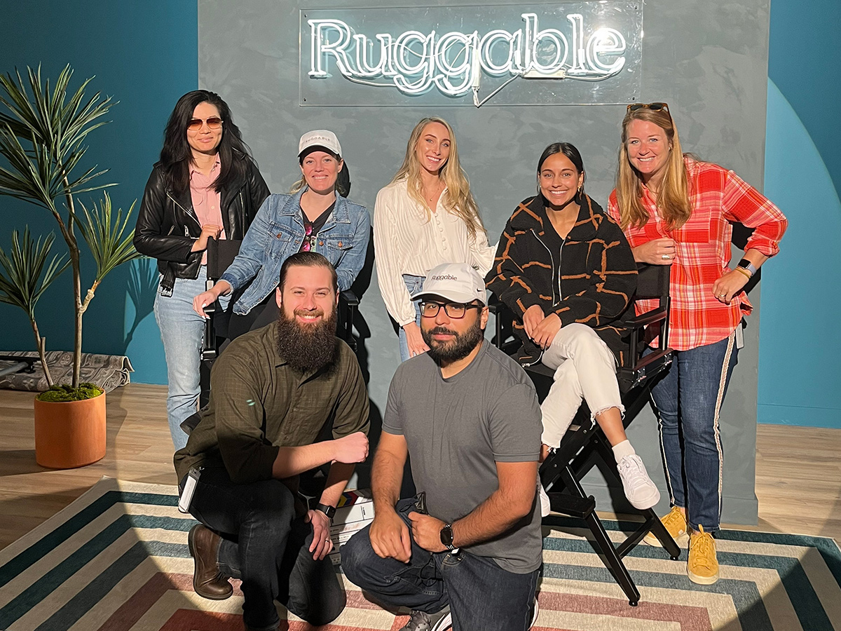 Team member group photo in the office with a neon Ruggable sign behind them