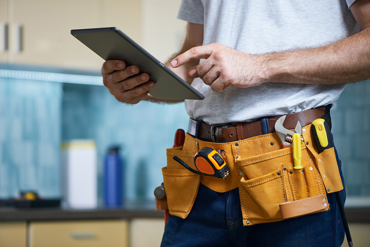 Cropped shot of young repairman wearing a tool belt with various tools using digital tablet