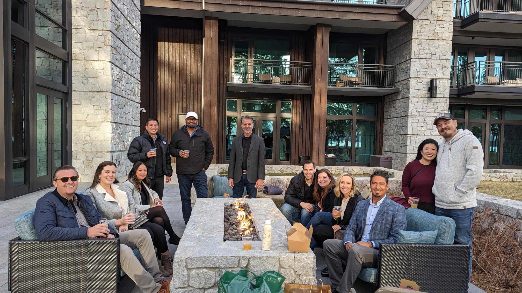 A group of Technossus employees sit around a fire outside.