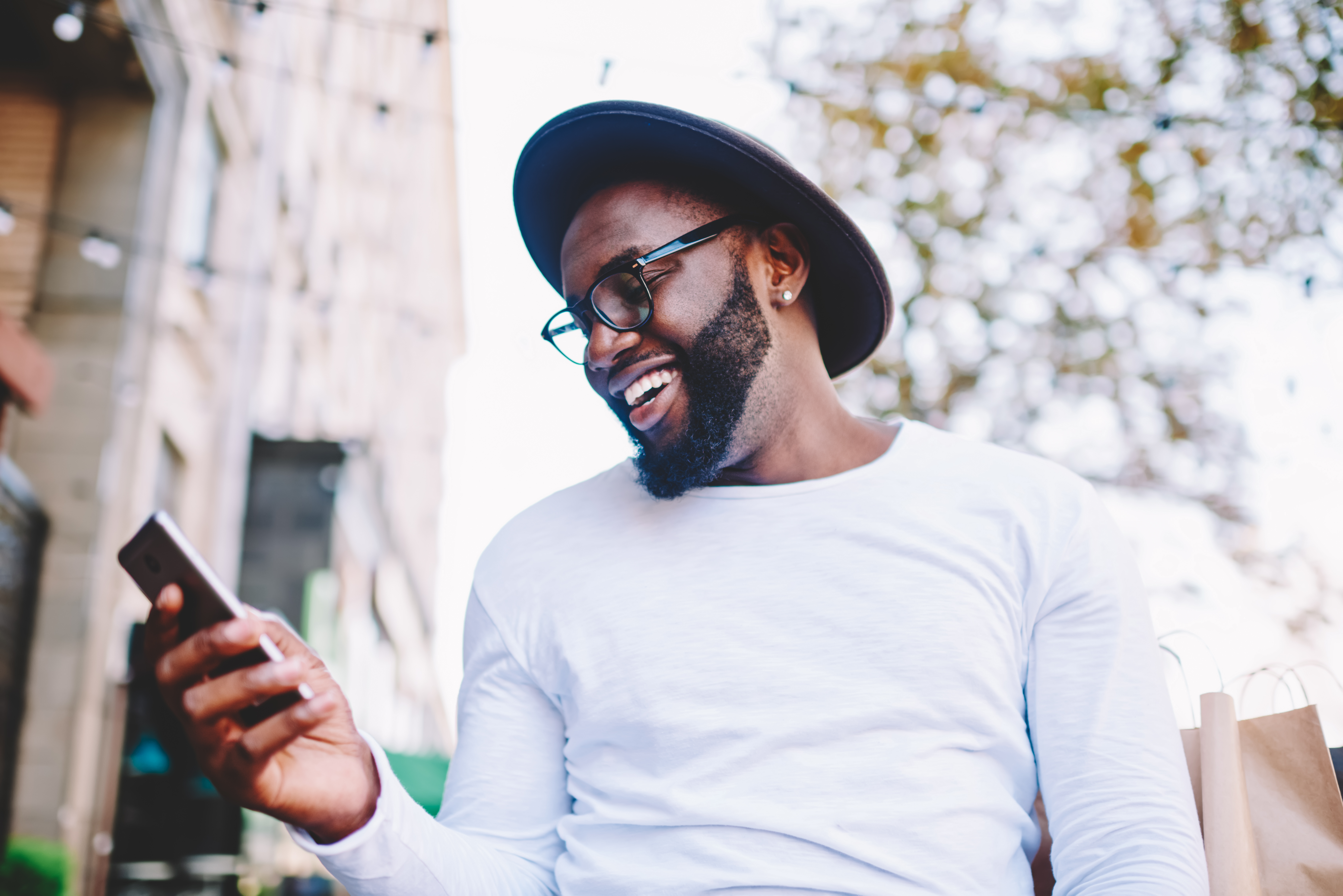 Stock photo of an African-American person with a beard looking at a mobile phone while walking own the street. 