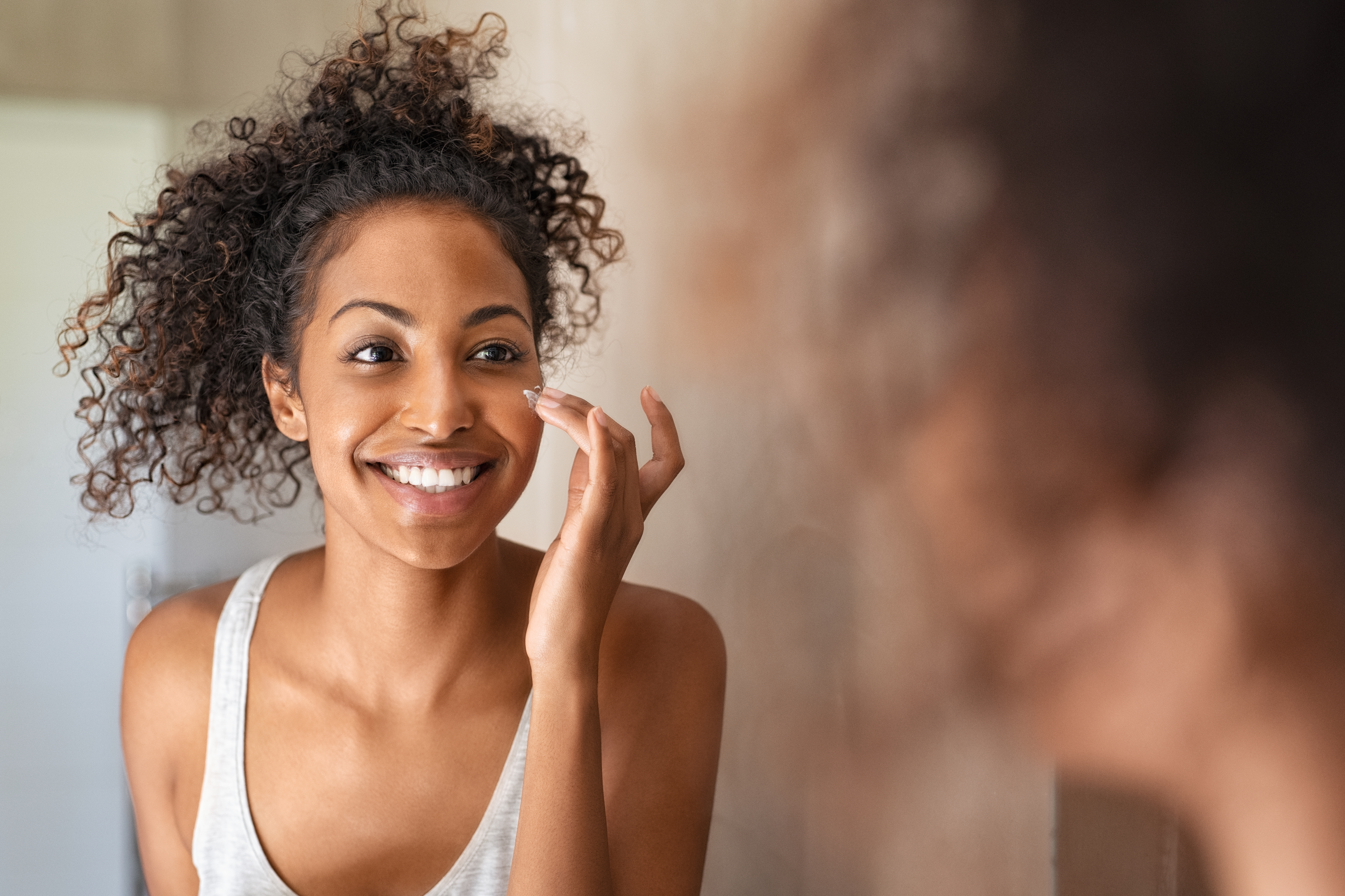 Stock photo of a young Black woman looking at herself in the mirror and smiling. 