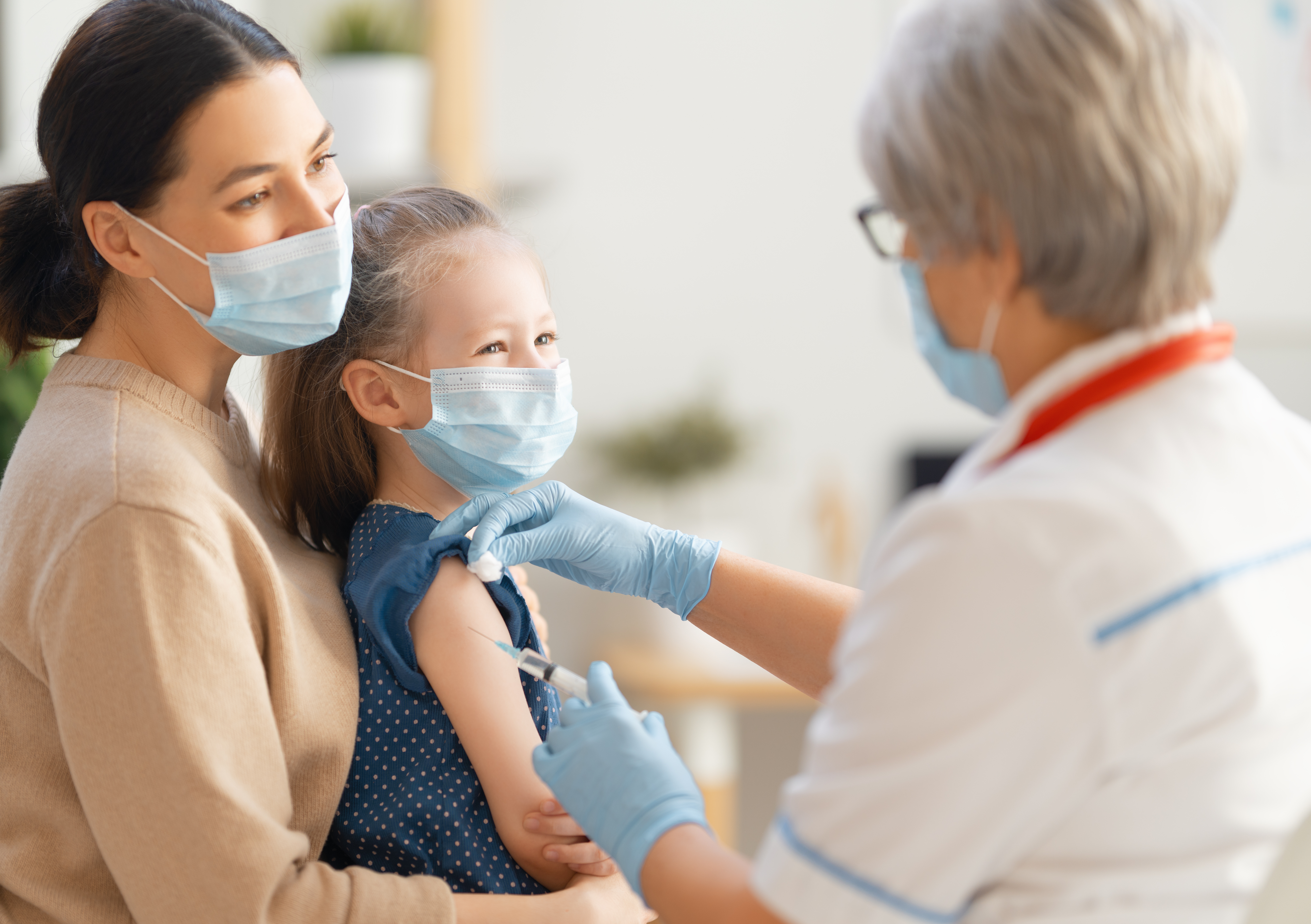 Stock photo of a parent and child with surgical masks on visiting an out-of-focus doctor.