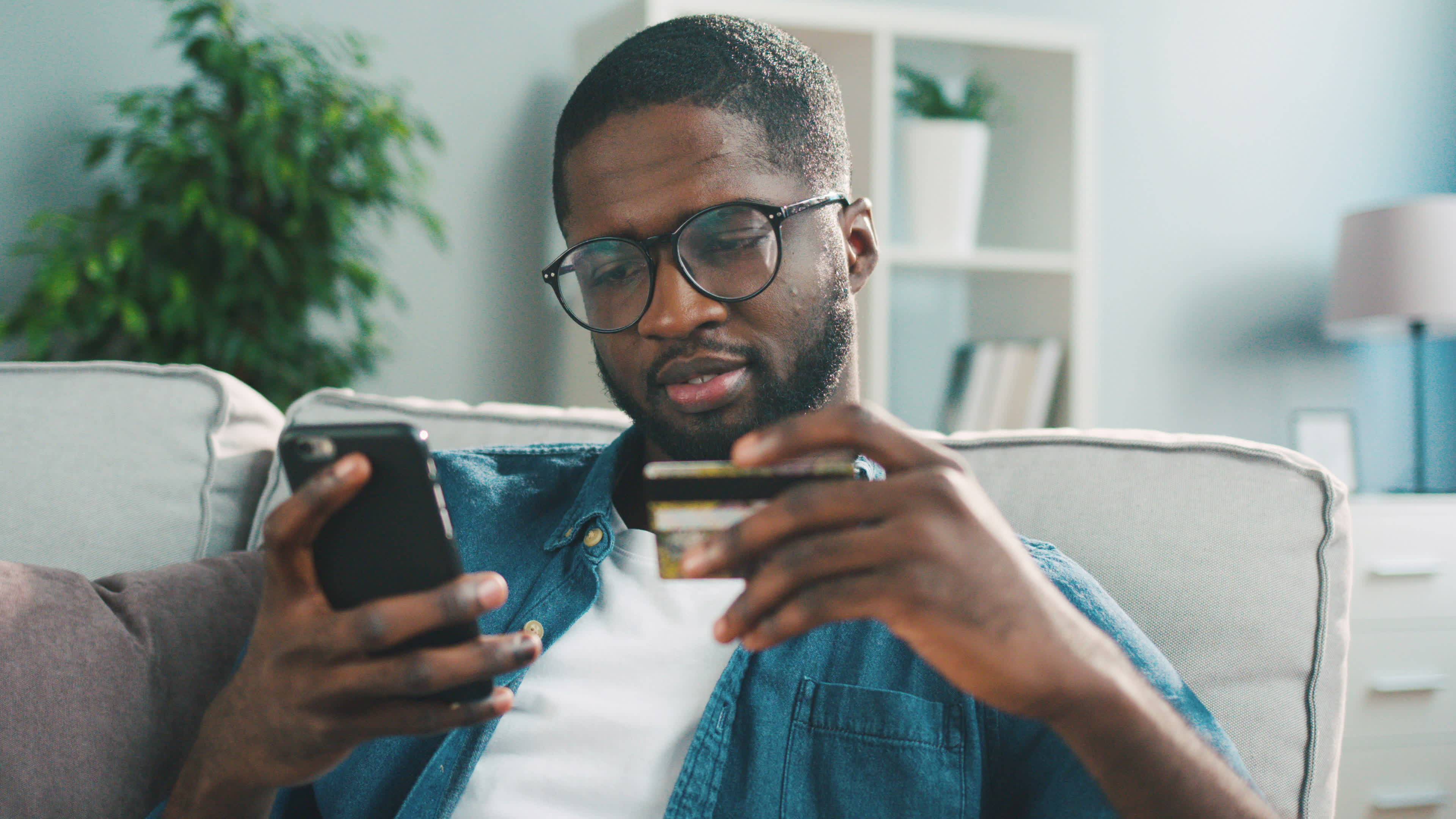 Stock photo of a Black man on his couch using his credit card to purchase something online. 
