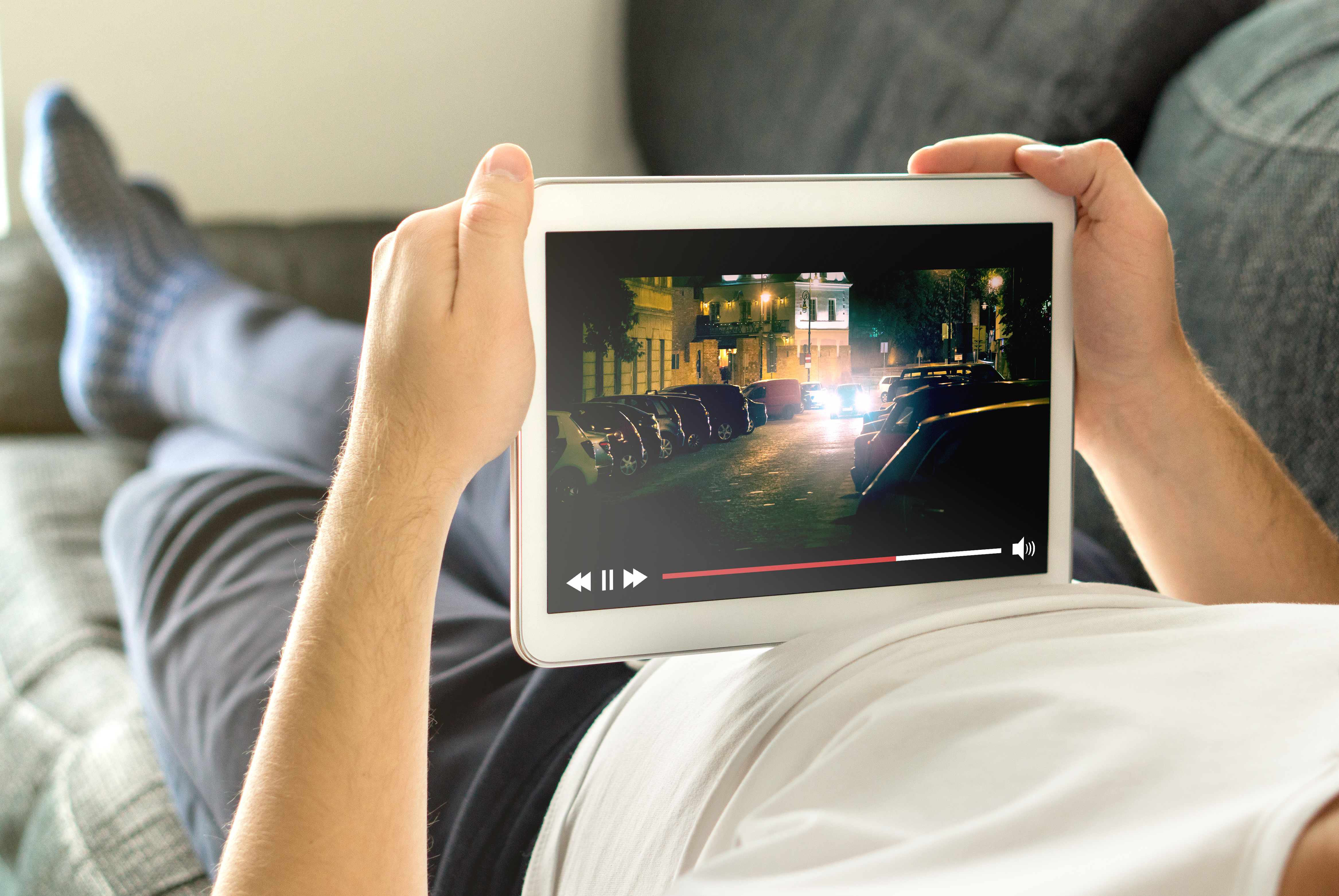 Stock photo of a person laying on the couch streaming a video on their tablet. 