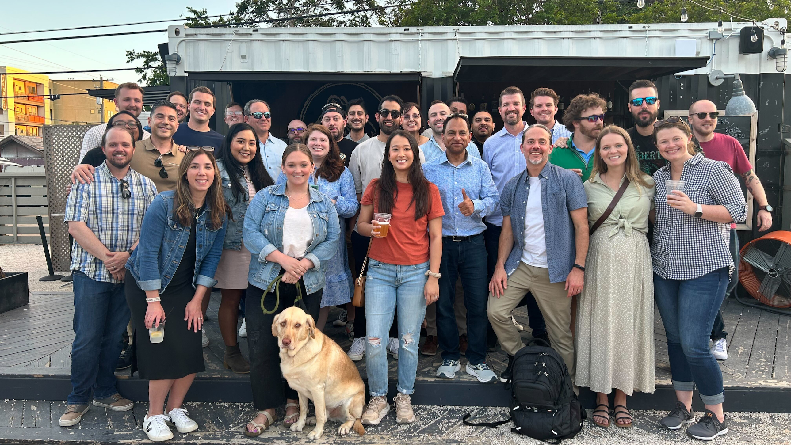 Large group photo of Redgate team members outside, with a dog in front. 