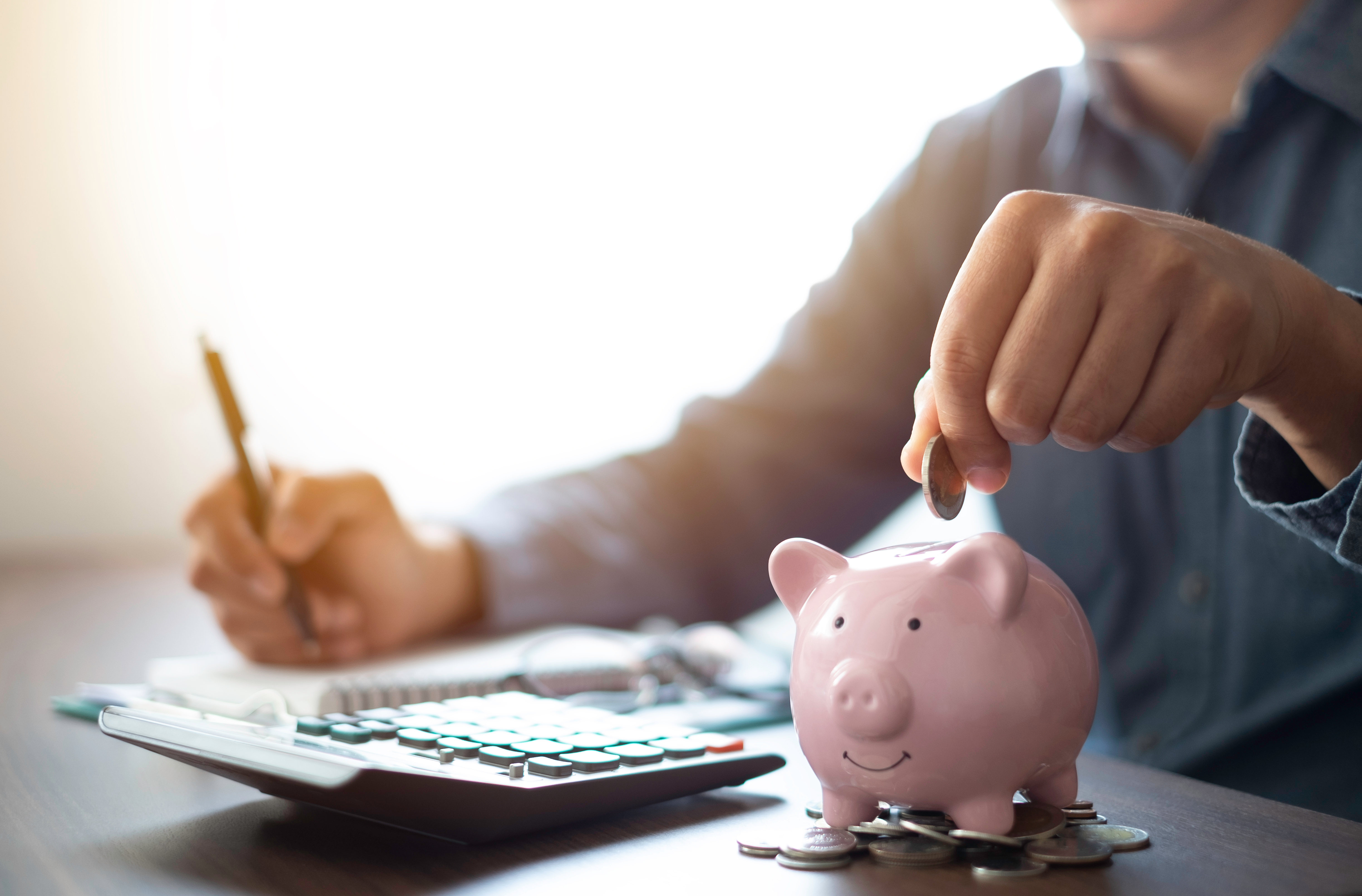 A man calculating his bill and adding money to a piggy bank.