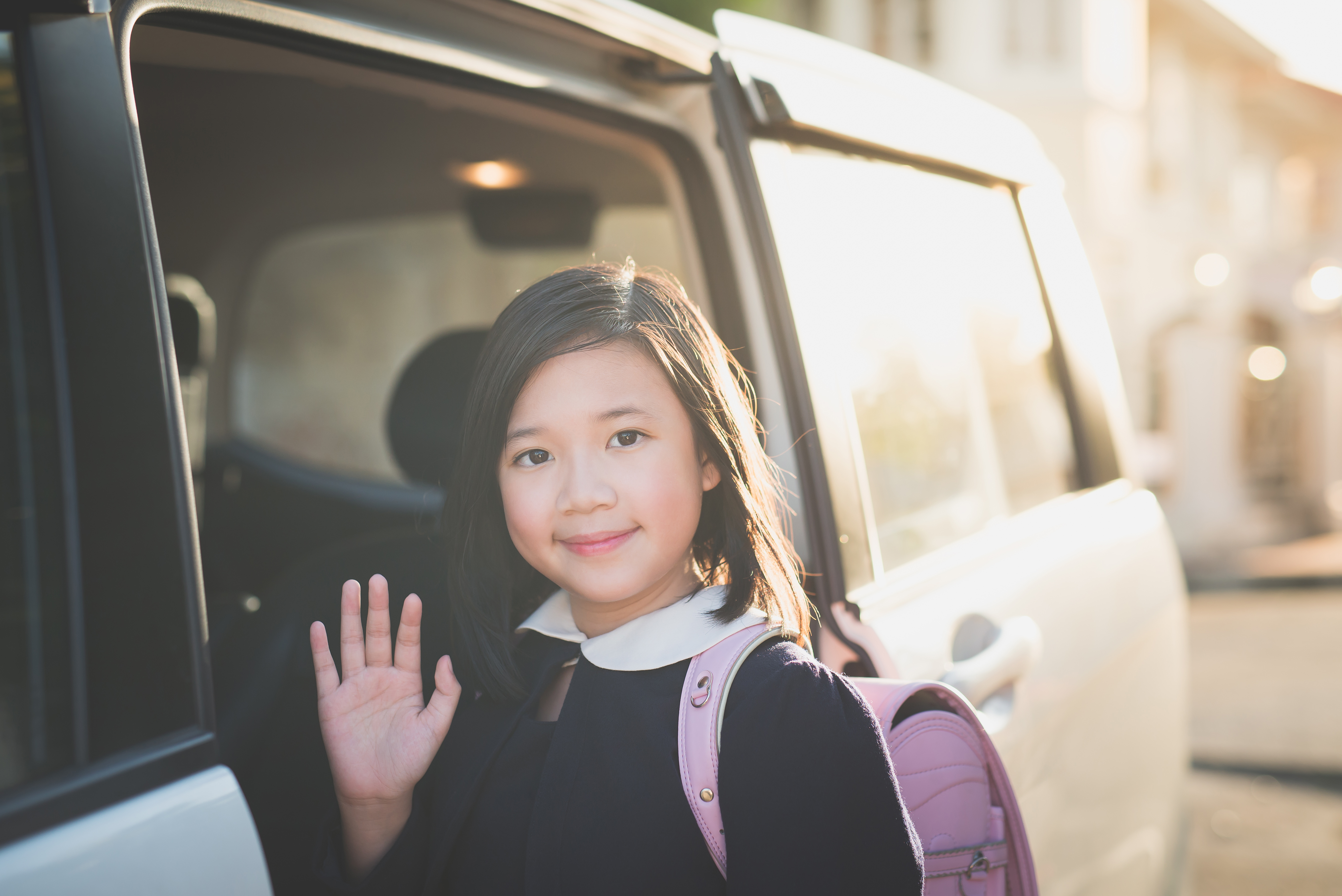 A child waves as she's being dropped off for school.
