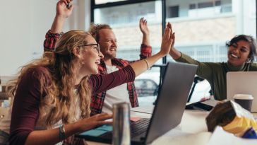 Image of three coworkers celebrating together over their laptops