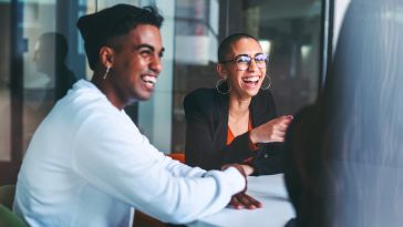 Two people smiling and laughing together in a conference room.