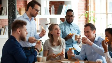 Colleagues talking, laughing and sharing a pizza in the office