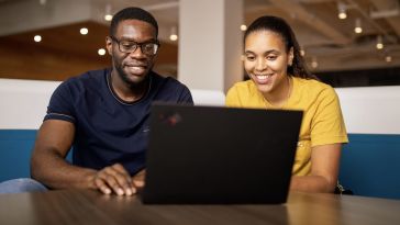 A man and a woman smile at a laptop computer