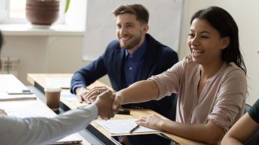 A Black woman smiles and shakes hands with someone across the table