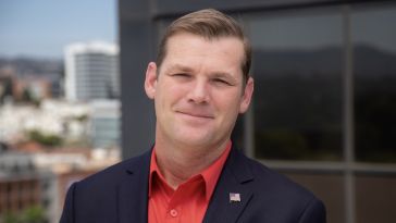 A man wears a red button up shirt and black blazer