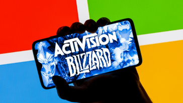 ctivision Blizzard logo on smartphone screen in hand against background of Microsoft logo. 