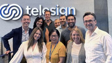 A group of Telesign employees stand together in front of the company sign.
