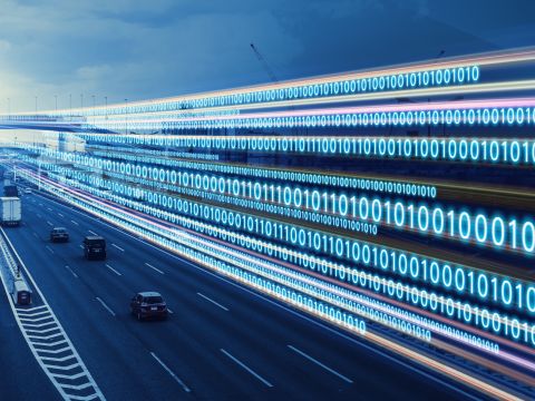 A blue-filtered photo of a highway with cars and trucks with binary code running alongside it, representing cybersecurity speed. 